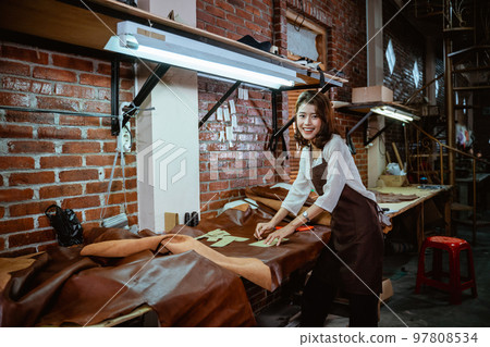 Tailor in apron smiling while measuring leather material at work Tailor in apron smiling while measuring leather material at work 97808534