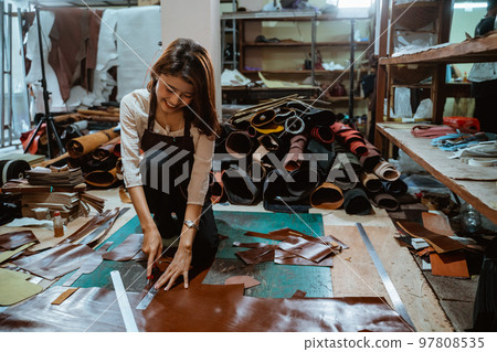 Asian craftswoman working cutting leather against leather material background Asian craftswoman working cutting leather against leather material background 97808535