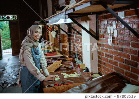 Female Asian hijabi tailor in apron smiling at camera Female Asian hijabi tailor in apron smiling at camera 97808539