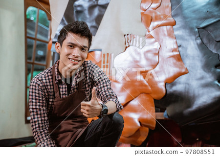 Smiling craftsman with thumbs up against leather materials background Smiling craftsman with thumbs up against leather materials background 97808551