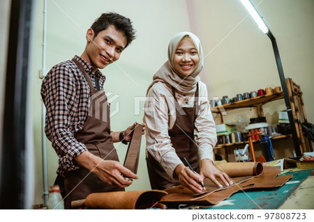 female craftsman with male craftsman smiling while measuring leather material 97808723