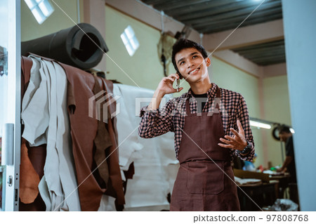 craftsman in apron making phone calls at leather workshop craftsman in apron making phone calls at leather workshop 97808768
