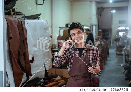 asian craftsman making calls with smartphone at leather craft workshop asian craftsman making calls with smartphone at leather craft workshop 97808776