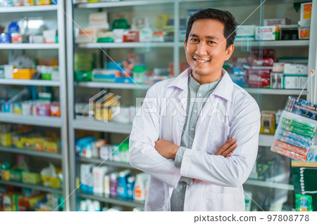 male pharmacist in uniform smiling with crossed hands on pharmacy male pharmacist in uniform smiling with crossed hands on pharmacy 97808778