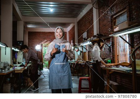 Smiling female leather craftsman with two thumbs standing in studio Smiling female leather craftsman with two thumbs standing in studio 97808780
