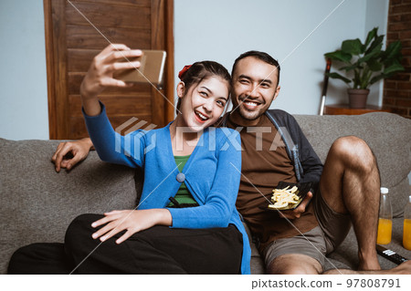woman holding smartphone for selfie with her boyfriend while sitting woman holding smartphone for selfie with her boyfriend while sitting 97808791