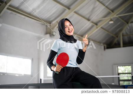 smiling hijabi female athlete holding paddle with thumbs up smiling hijabi female athlete holding paddle with thumbs up 97808813