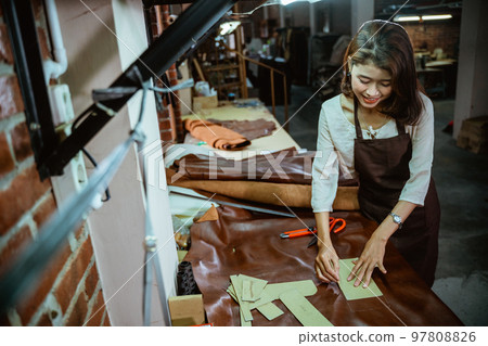 Craftwoman working with leather making basic shapes on a workbench 97808826
