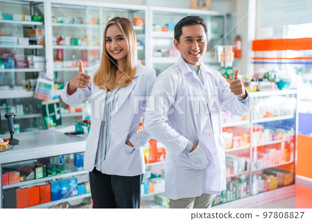 Two smiling asian female and male pharmacists with thumbs up 97808827