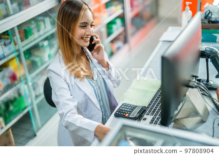 Attractive female pharmacist working in while making phone call Attractive female pharmacist working in while making phone call 97808904