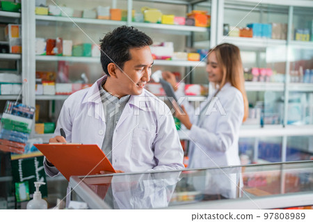 male pharmacist in uniform working checking medicine in a window male pharmacist in uniform working checking medicine in a window 97808989