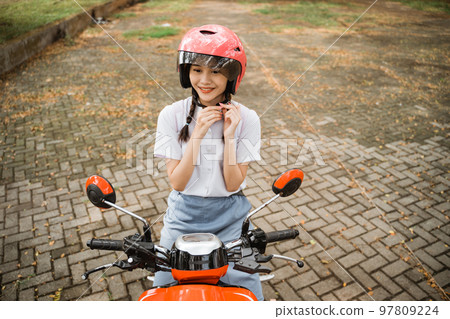 Student girl tightens rope while wearing helmet on motorbike 97809224