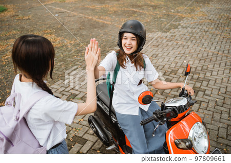 Student girl clapping hands with friend while riding a motorcycle 97809661