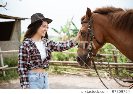 woman in cowboy hat stroking the head of a horse 97809764