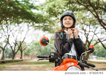 High school girl tightens helmet strap while riding motorbike 97809765