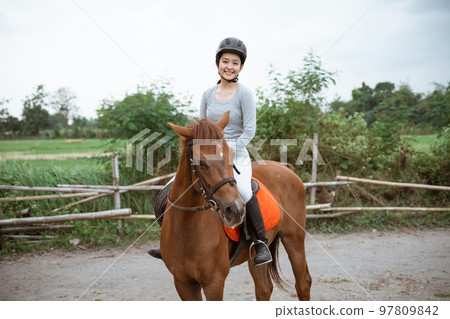 Female equestrian smiling while riding horse and holding reins 97809842