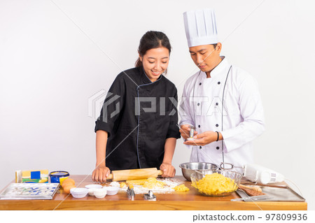 male and female chefs using a rolling pin male and female chefs using a rolling pin 97809936