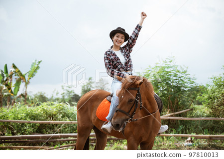 woman in cowboy hat sitting on horse with fist up 97810013