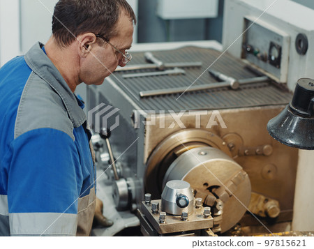 Turner in overalls works behind lathe in production hall. Processing of metal products. background.. Turner in overalls works behind lathe in production hall. Processing of metal products. background.. 97815621