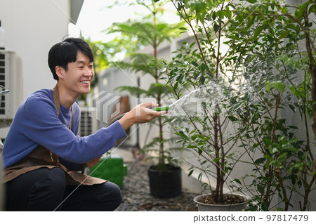 Man watering plants from hose, taking care of plants in garden. Gardening hobby concept Man watering plants from hose, taking care of plants in garden. Gardening hobby concept 97817479
