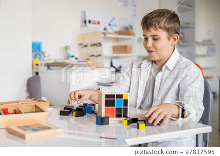 Happy male kid assembling Montessori material trinomial cube at school classroom desk Happy male kid assembling Montessori material trinomial cube at school classroom desk 97817595