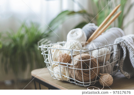 Cozy homely atmosphere. Female hobby knitting. Yarn in neutral colors in a white iron wire basket. 97817676