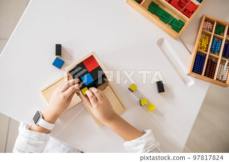 Childish male hands assembling trinomial cube wooden Montessori material on desk closeup top view Childish male hands assembling trinomial cube wooden Montessori material on desk closeup top view 97817824