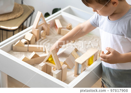 Cute boy kid playing sensory box kinetic sand table with Montessori wooden materials Cute boy kid playing sensory box kinetic sand table with Montessori wooden materials 97817908
