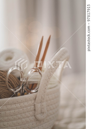 Cozy homely atmosphere. Female hobby knitting. Yarn in neutral shades in a soft basket of white 97817915