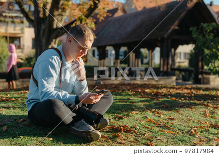 Professional Photographer Taking Picture Of Beautiful Autumn Park. Man Professional Photographer Sit With Camera And With Smartphone In Autumn Park. Retouched, Vibrant Colors, Brownish Tones. Professional Photographer Taking Picture Of Beautiful Autumn Park. Man Professional Photographer Sit With Camera And With Smartphone In Autumn Park. Retouched, Vibrant Colors, Brownish Tones. 97817984