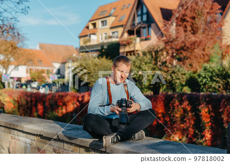 Man Sitting in Old European City And Holding Photo Camera. Contemporary Stylish Blogger And Photographer. Handsome man taking a selfie on a trip in Europe. Man Sitting in Old European City And Holding Photo Camera. Contemporary Stylish Blogger And Photographer. Handsome man taking a selfie on a trip in Europe. 97818002