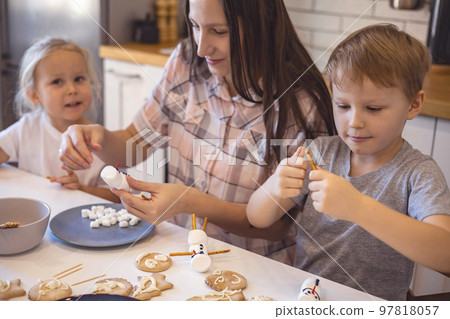 Mom and kids make snowmen from marshmallows. They drink cocoa and get ready for Christmas. Christmas home concept. Mom and kids make snowmen from marshmallows. They drink cocoa and get ready for Christmas. Christmas home concept. 97818057