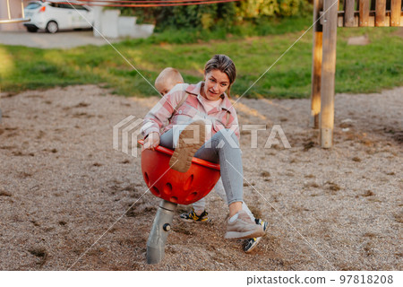 Mother and son having fun on a swing. Motherhood and childhood concept. Sunny summer day. Beautiful family is having fun outside. Parents with children riding on a swing. Mom is playing with her Mother and son having fun on a swing. Motherhood and childhood concept. Sunny summer day. Beautiful family is having fun outside. Parents with children riding on a swing. Mom is playing with her 97818208