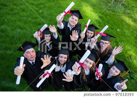 Graduates in robes show off their diplomas outdoors. View from above. Age student. 97818393