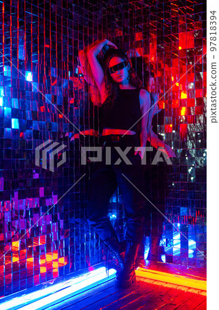 Portrait of a caucasian woman in sunglasses in neon light against a mirror wall.  97818394