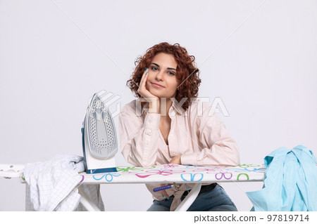 The girl leans her elbow against the ironing board and her hand against her head. 97819714