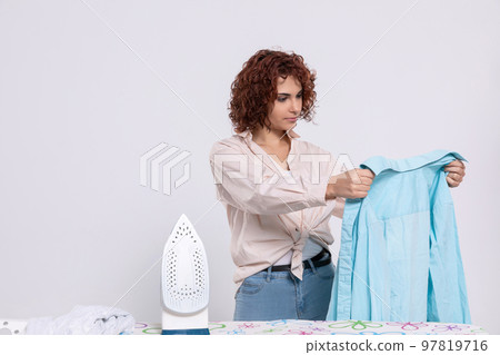 Before ironing, the girl carefully inspects the shirts. Before ironing, the girl carefully inspects the shirts. 97819716