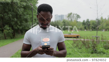 African american man orders food in an online store using a smartphone. Male using a food delivery app. Online delivery, online store, home delivery. African american man orders food in an online store using a smartphone. Male using a food delivery app. Online delivery, online store, home delivery. 97824832