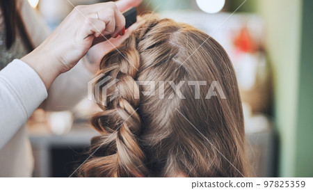 The girl makeup artist makes a braid for the model. 97825359