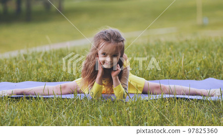 The little girl performs an element of rhythmic gymnastics - splits in the park. 97825360