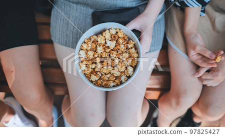Friends eating popcorn on the street. Close-up of hands. 97825427