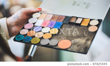 The makeup artist is holding a palette of shadows. 97825445