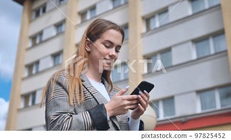 A girl walks through town and looks at her smartphone. 97825452