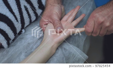 A masseur massages the wrists of a girl. 97825454