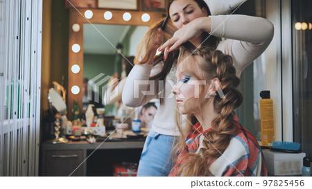 The girl makeup artist makes a braid for the model. The girl makeup artist makes a braid for the model. 97825456