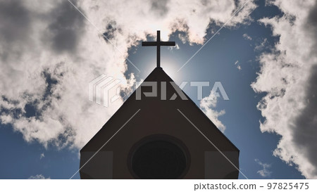 The silhouette of a Catholic church tower against a background of sun and clouds. 97825475