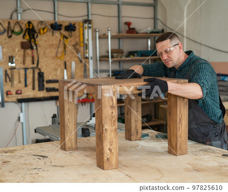 Male carpenter finishing work on wooden table in workshop. Male carpenter finishing work on wooden table in workshop. 97825610