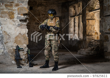 A woman in an army uniform holds a firearm in an abandoned building. A woman in an army uniform holds a firearm in an abandoned building. 97825611