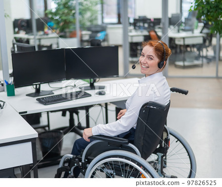Caucasian woman with headset in a wheelchair. Female call center worker in the office. 97826525