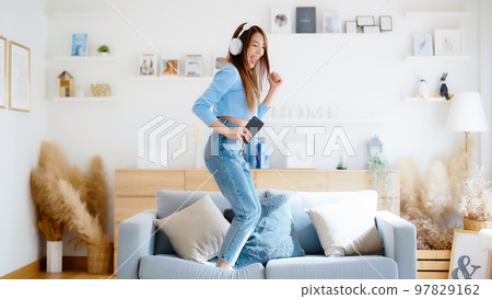 On the sofa in her living room, a young Asian woman dances 97829162